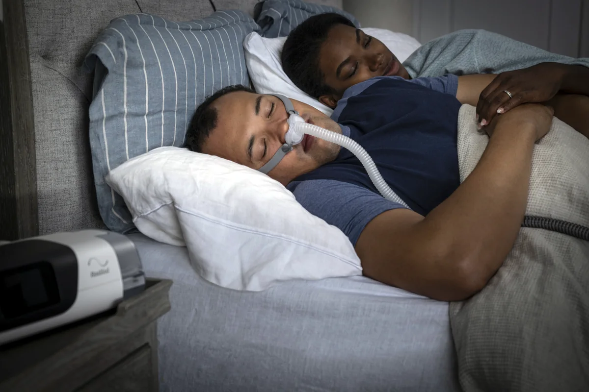 Pessoa dormindo com máscara de CPAP conectada a equipamento ResMed AirSense 11